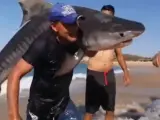 'Aquaman mexicano': un hombre sale del mar con un tiburón en brazos bajo la atenta mirada de los presentes en la playa.
