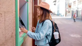Una joven turista española sacando dinero de un cajero en el extranjero.