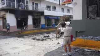 Personas toman fotografías a locales incendiados este lunes, en Puerto Vallarta (México).