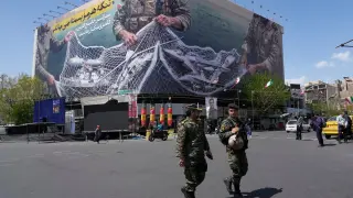 Dos agentes de policía caminan frente a una valla publicitaria antiestadounidense que muestra aviones estadounidenses cayendo en la red de pesca de las fuerzas armadas iraníes, con letreros en persa que dicen