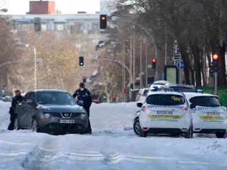 Dos polic&iacute;as municipales empujan un coche que ha quedado atrapado entre el hielo y la nieve, en una calle de Madrid.