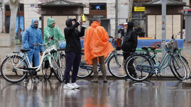 Varias personas se protegen de la lluvia con chubasqueros por las calles de Valencia, este domingo.