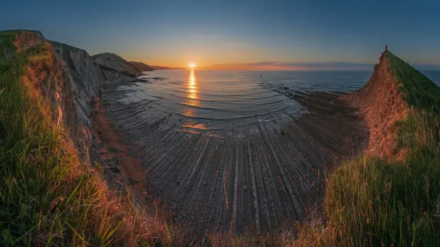 Solo cuando la marea está baja podemos visitar esta playa de Deba, la más salvaje del Geoparque de la Costa Vasca, protegida, entre dos cabos, por un acantilado a cuyos pies se extiende una de las mayores rasas mareares de Europa, con los estratos del flysch arañando la memoria de la Tierra desde hace más de 50 millones de años. deba.eus