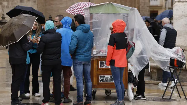 Varias personas se protegen este domingo de la lluvia con chubasqueros y paraguas por las calles de Valencia.