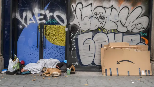 Una persona sin hogar duerme en Passeig de Gràcia de Barcelona junto a su perro.