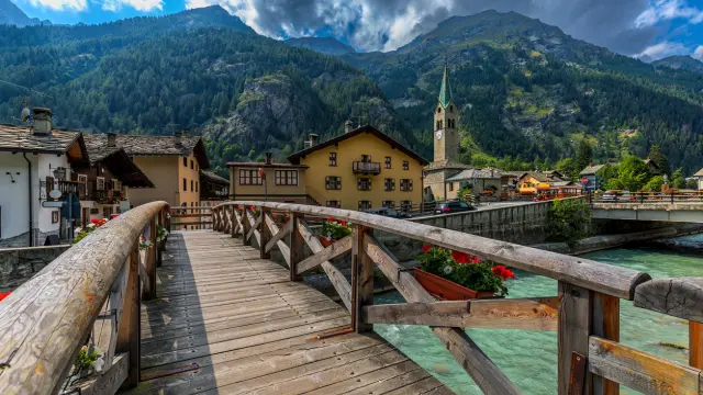 Wooden bridge over mountain river as houses and old church on background in small town of Gressoney-Saint-Jean in Aosta Valley, Italy.