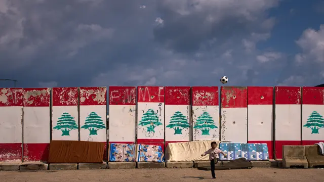 Un niño, desplazado con su familia de los suburbios del sur de Dahiyeh, juega con una pelota junto a colchones empapados por la lluvia que se secan al sol en Beirut.