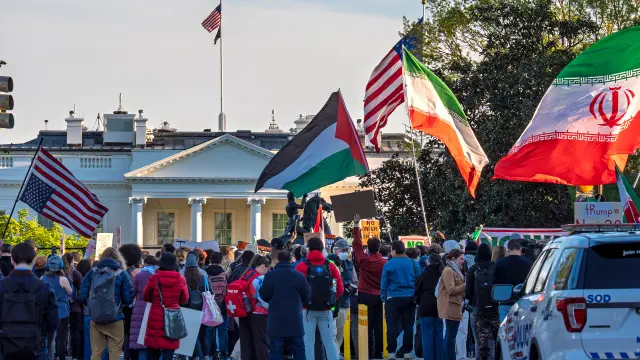 Protestors wave flags near the White House in Washington, Tuesday evening, April 7, 2026. (AP Photo/J. Scott Applewhite)
