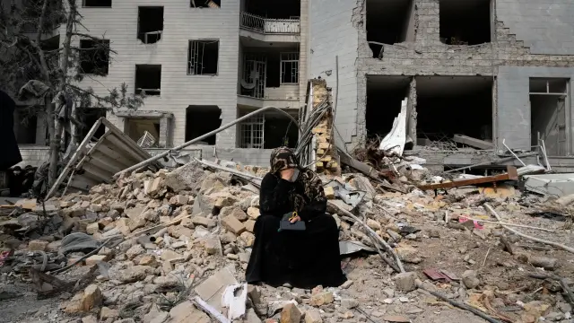 Una mujer se sienta sobre los escombros frente a un edificio residencial dañado por un bombardeo estadounidense-israelí en Teherán, Irán.