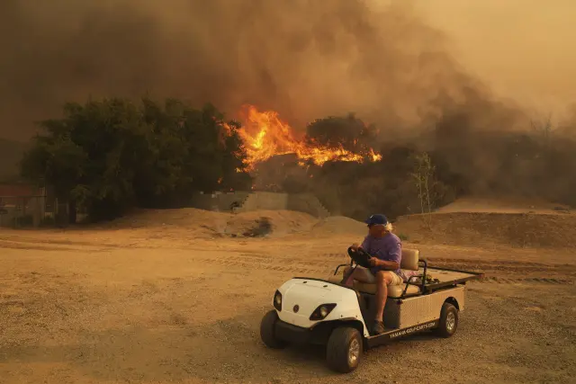 A resident rides a golf cart as he exits his property while the Canyon Fire burns on Thursday, Aug. 7, 2025, in Hasley Canyon, Calif. (AP Photo/Marcio Jose Sanchez)