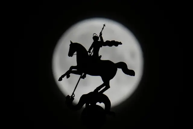 The full moon rises behind the statue of St. George atop a building in Moscow on early Thursday, April 2, 2026. (AP Photo/Pavel Bednyakov)