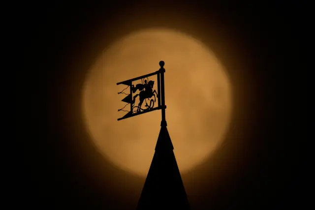 The full moon rises behind a weather vane portraying St. George atop the Baltschug Hotel, in Moscow, early Thursday, April 2, 2026. (AP Photo/Pavel Bednyakov)