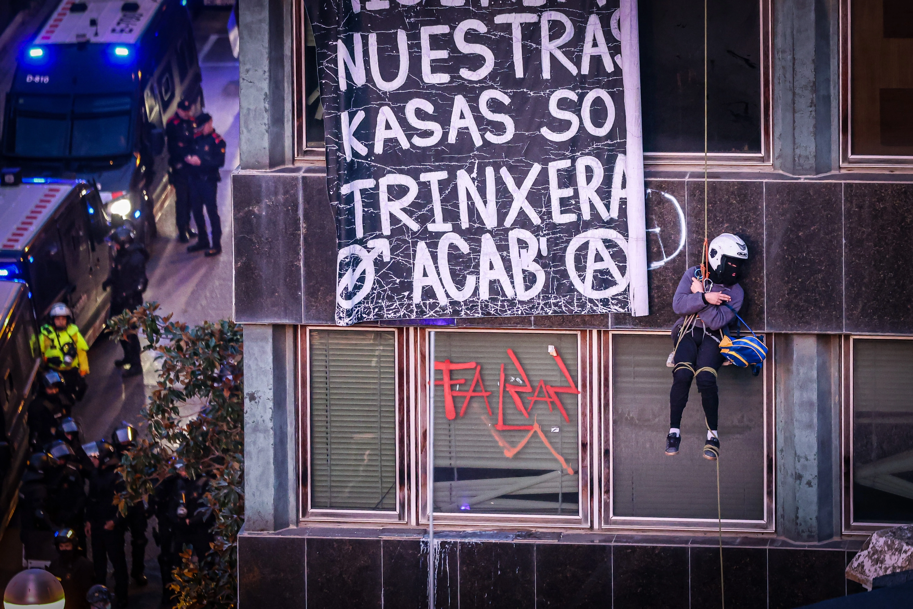 Un okupa permanece colgado de una de los edificios de la plaza de Bonanova, en Barcelona, durante el desalojo que están llevando a cabo los Mossos.