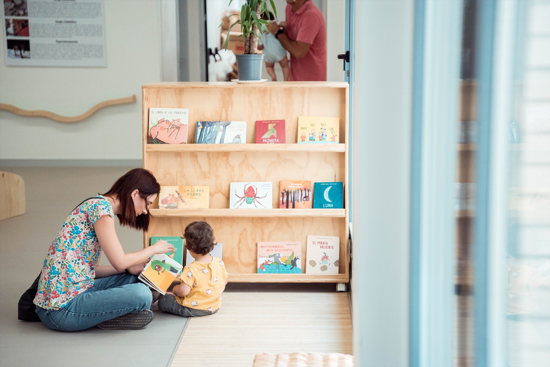Una mujer junto a un niño cogen libros de una estantería de la Escuela Infantil Municipal Las Golondrinas, en Madrid.