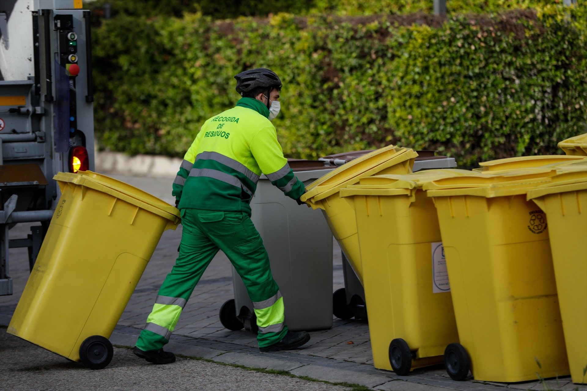 OPERIO DE RECOGIDA DE REDUUOS TRASLADA DOS CUBOS DE BASURA AMARILLOS DESTINADOS A ENNEÇÕES EM UNA CALLE DE MADRID.