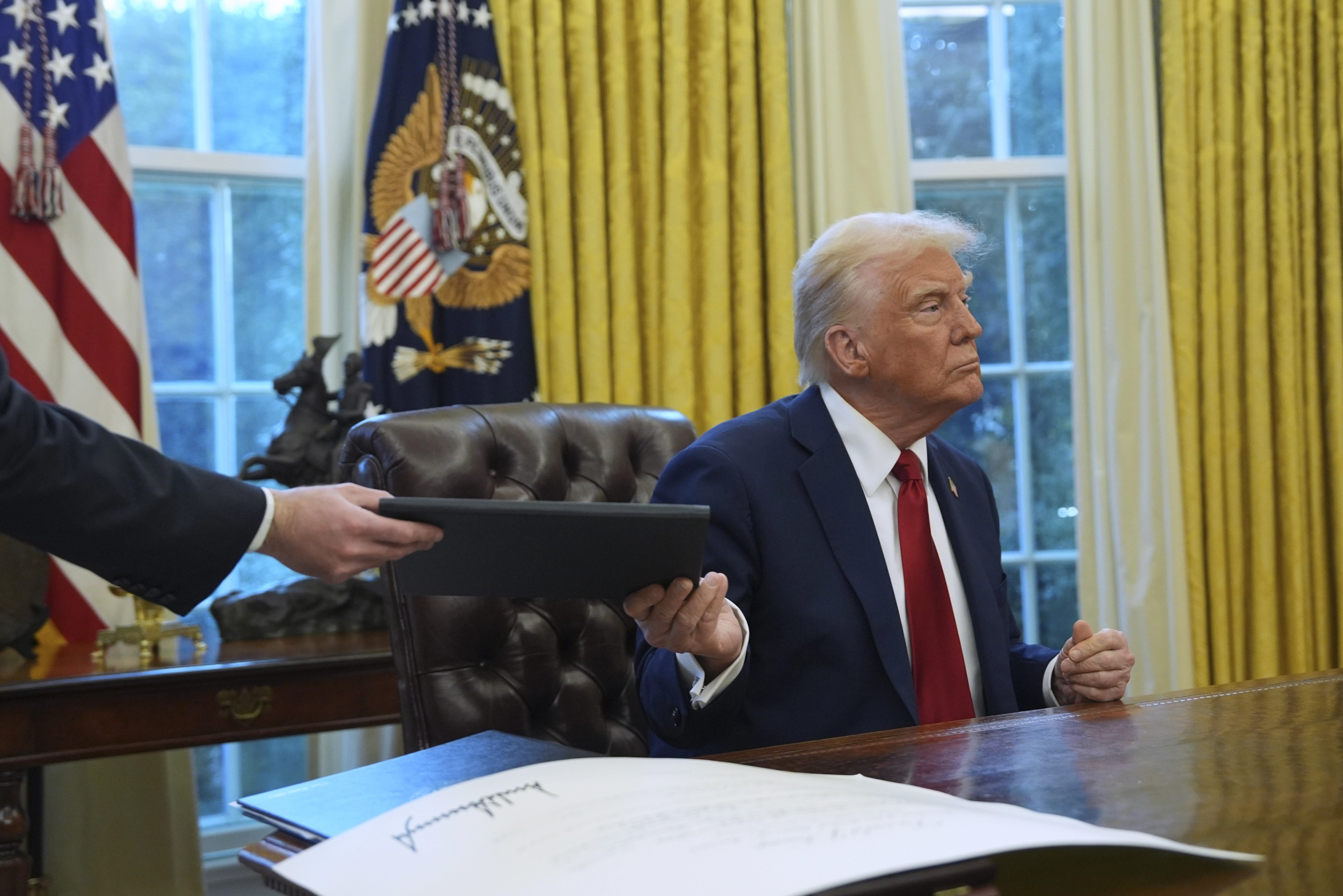 El presidente de EE UU, Donald Trump, entrega una orden ejecutiva firmada al secretario del personal de la Casa Blanca, Will Scharf, en el Despacho Oval.