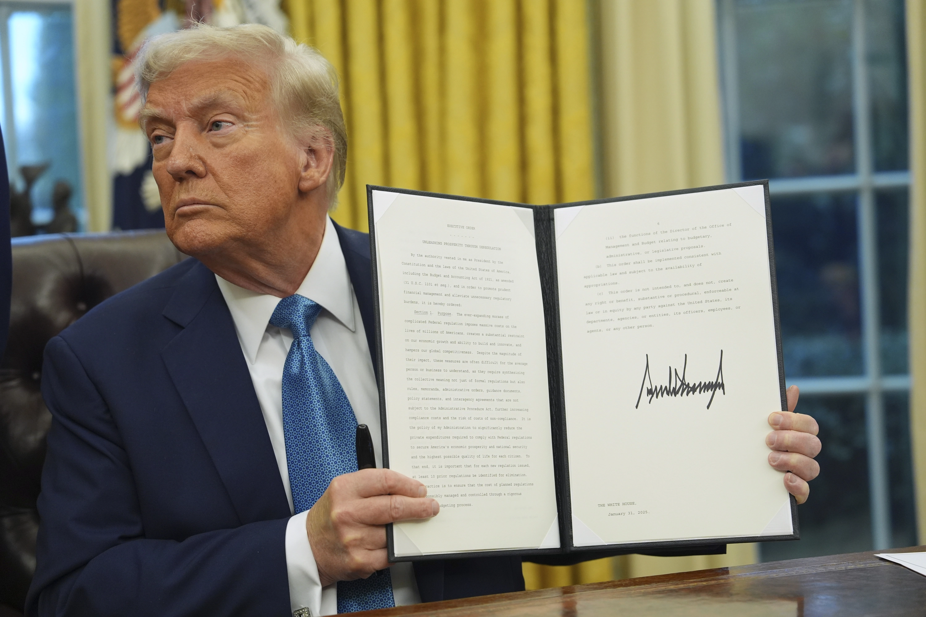 El presidente Donald Trump sostiene una orden ejecutiva firmada decretos en el Despacho Oval de la Casa Blanca.