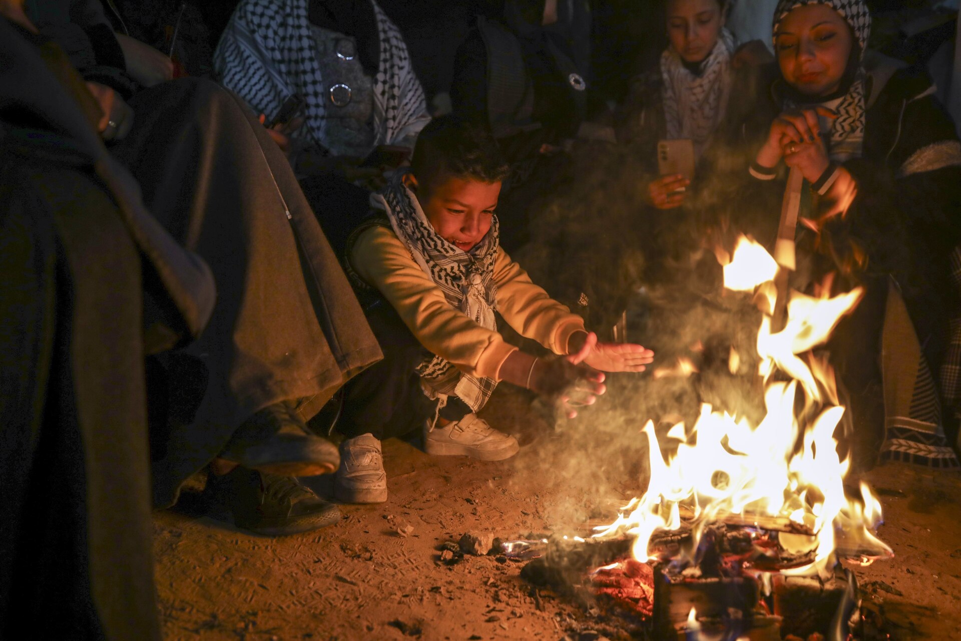 A boy warms up as families and friends of Palestinian prisoners to be released from Israeli prison wait around a bonfire for their arrival in Khan Younis, southern Gaza Strip, late Wednesday Feb. 26, 2025. (AP Photo/Jehad Alshrafi)