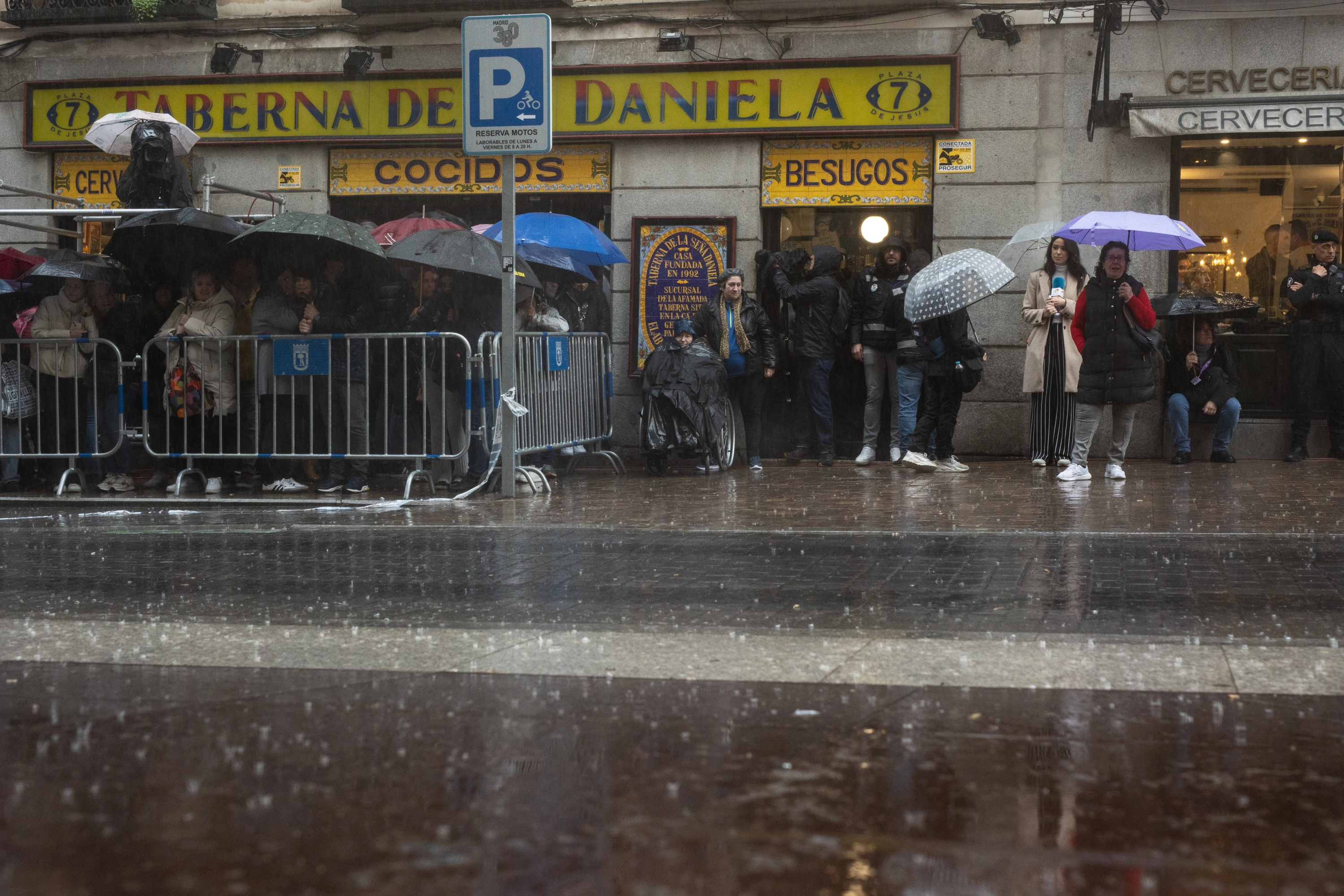 Varias personas aguardan bajo la lluvia para ver si sale una procesión esta Semana Santa en Madrid.