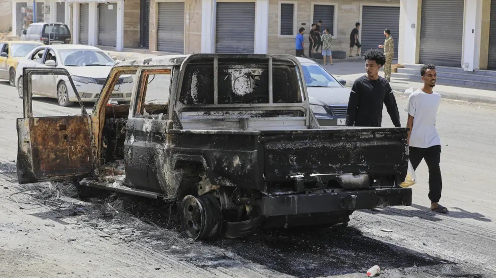 Dos ciudadanos caminan junto a un camión quemado, en Trípoli (Libia).